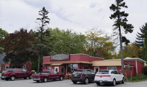 A red building with a sign reading "Satur's" surrounded by trees and parked cars on a cloudy day.