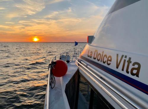 A boat named "La Dolce Vita" sails on calm waters at sunset, with vibrant colors in the sky.