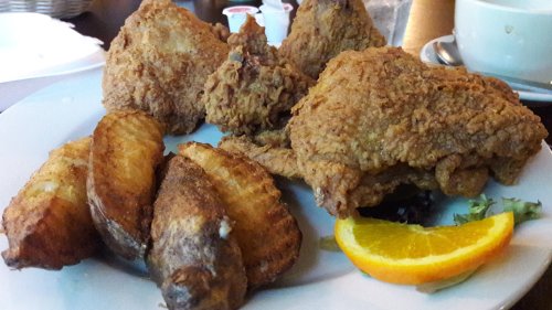 A plate of crispy fried chicken pieces with golden-brown fried potatoes and a slice of orange.