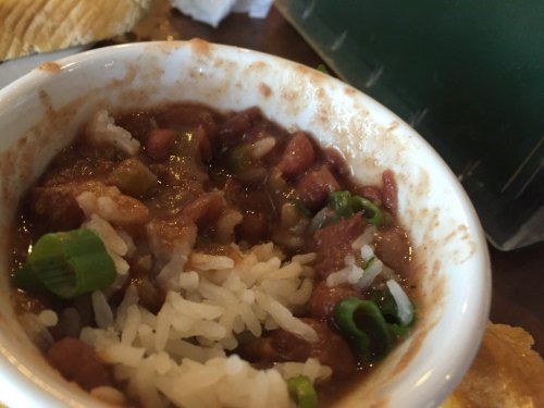 A small bowl of beans and rice topped with chopped green onions, served on a wooden table.
