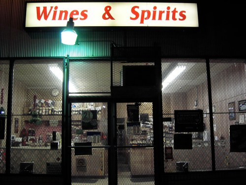 A storefront with a sign reading "Wines & Spirits," illuminated at night, featuring a gated entrance.