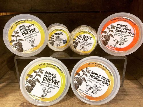 Five varieties of artisan cheese in round containers, labeled with flavors like garlic, red pepper, and apple cider.