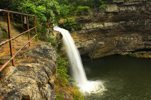 A serene waterfall cascades into a tranquil pool, surrounded by lush greenery and rocky cliffs.
