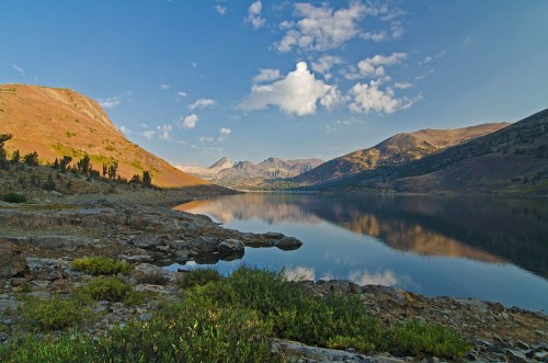 Scenic view of a calm lake surrounded by mountains and blue sky, with reflections on the water's surface.