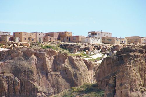 A hillside village with stone and adobe buildings, set against rocky terrain under a clear blue sky.