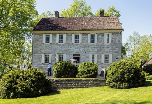 A historic stone house surrounded by greenery, with visitors at the entrance on a sunny day.