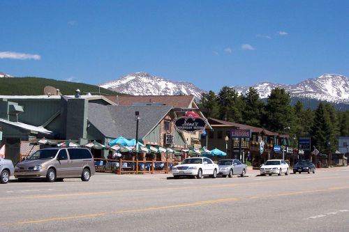 A scenic view of a mountain town with shops, outdoor seating, and snow-capped mountains in the background.