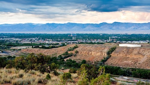 A panoramic view of a valley with mountains in the background, featuring a small town and cloudy skies.