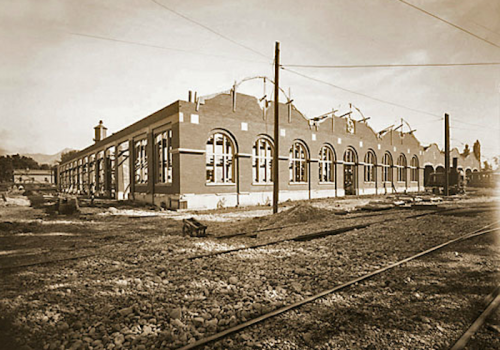 Historic building under construction, featuring arched windows and a railway track in the foreground.