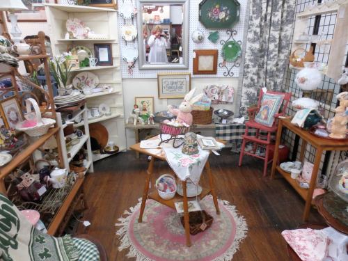 A cozy vintage shop corner filled with antiques, decorative items, and a small table with a lace tablecloth.