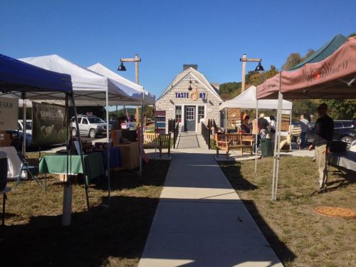 A view of a market with tents and booths, leading to a building labeled "Taste." Clear blue sky above.