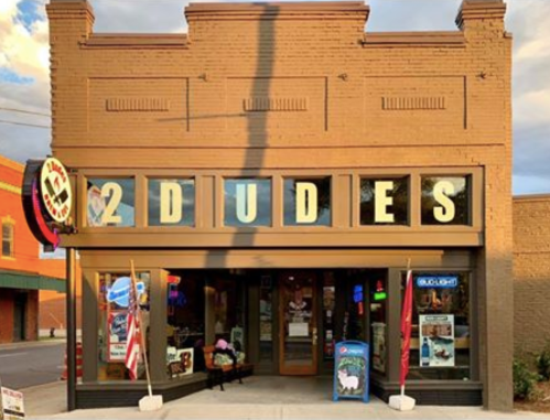 Exterior of a building with the sign "2 DUDES," featuring colorful lights and flags outside.