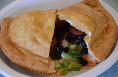 A golden-brown calzone filled with pepperoni, olives, and green peppers, partially opened on a white plate.