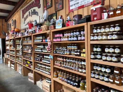 A rustic store interior featuring wooden shelves filled with various jars of preserves, sauces, and canned goods.