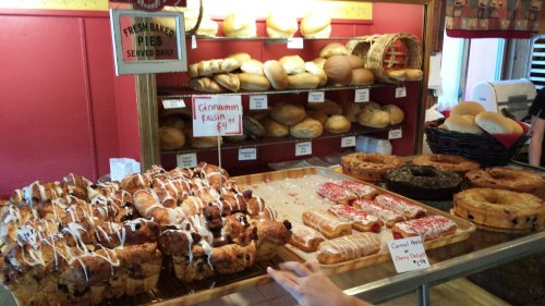 A display of fresh baked goods, including cinnamon raisin rolls, donuts, and various breads on a tray.