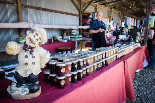 A market stall with jars of jam lined up, featuring a chef statue and a vendor in the background.