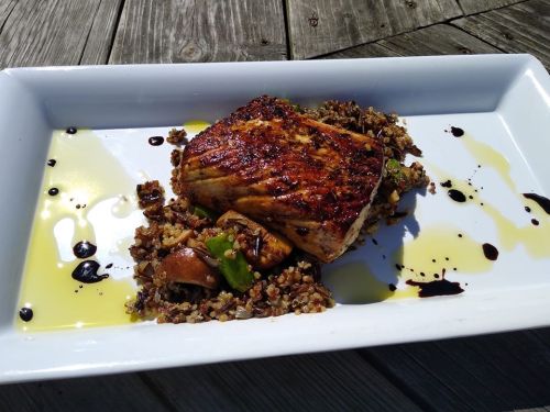 Grilled fish fillet on a bed of quinoa and vegetables, drizzled with olive oil and balsamic reduction.