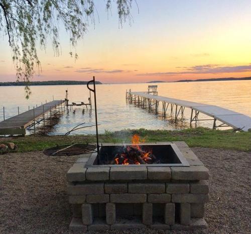 A serene lakeside view at sunset, featuring a fire pit and wooden docks extending into the calm water.