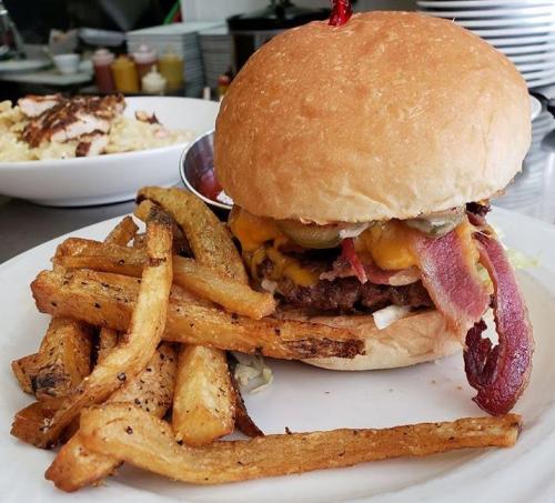 A juicy burger with cheese, bacon, and pickles, served with crispy fries on a white plate.