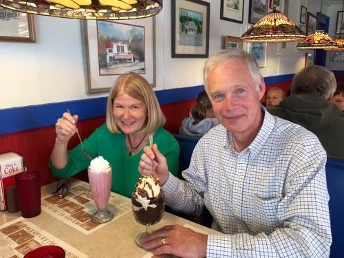 A man and woman enjoy ice cream sundaes at a cozy diner, smiling and holding their desserts.