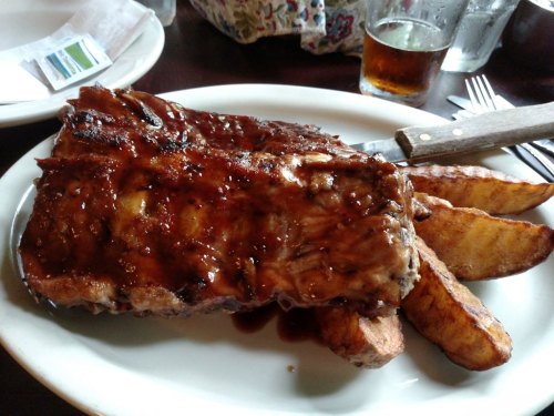 A plate of barbecue ribs glazed with sauce, served with golden-brown potato wedges.