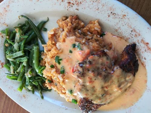 A plate featuring seasoned fish with creamy sauce, cornbread stuffing, and green beans on the side.