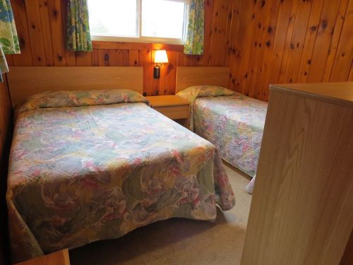 Cozy bedroom with two twin beds, wooden walls, floral bedspreads, and a window with curtains.