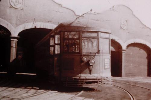 A vintage tram parked in an archway of a station, with tracks leading into the building.