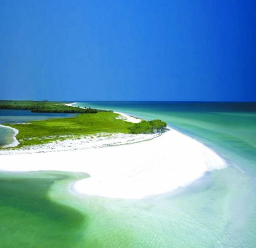 A serene coastal landscape featuring white sandy shores, lush greenery, and calm turquoise waters under a clear blue sky.