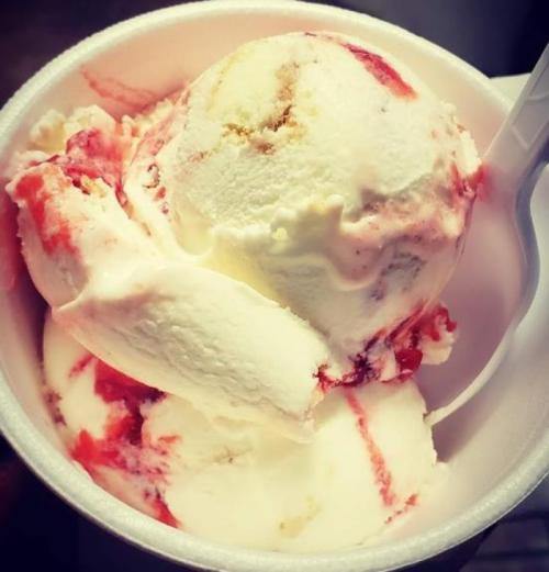 A cup of ice cream with swirls of strawberry sauce and a scoop of vanilla and cake-flavored ice cream.
