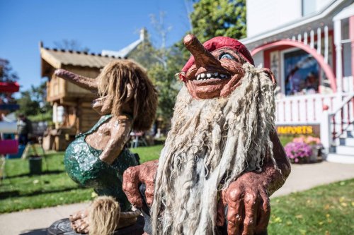 Two whimsical troll sculptures with exaggerated features, one with a long nose and the other with wild hair, in a sunny outdoor setting.