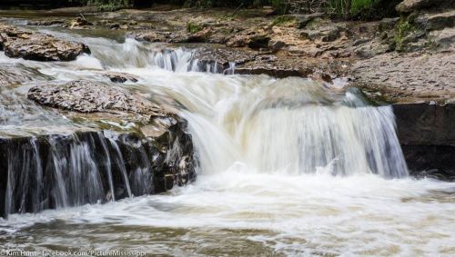 A serene waterfall cascading over rocky terrain, surrounded by lush greenery.