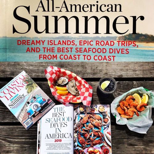 A table with seafood dishes, magazines, and a coastal background, featuring an "All-American Summer" theme.