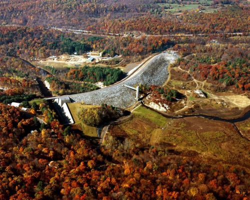Aerial view of a dam surrounded by vibrant autumn foliage and a winding river below.