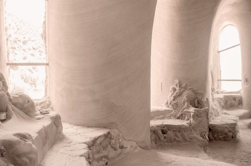 A minimalist, sandy-toned interior with curved walls and natural light filtering through windows.