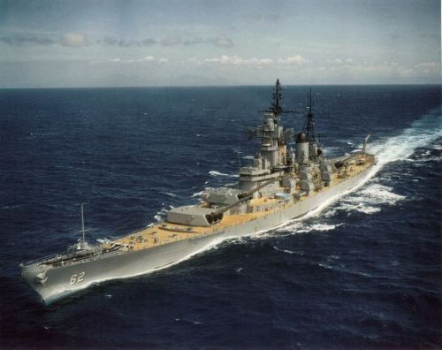 A large battleship sailing through open water, with a clear sky and gentle waves in the background.