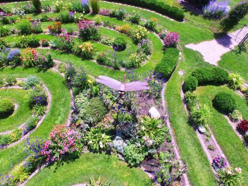 Aerial view of a vibrant garden with spiral paths, colorful flowers, and a decorative dragonfly sculpture in the center.