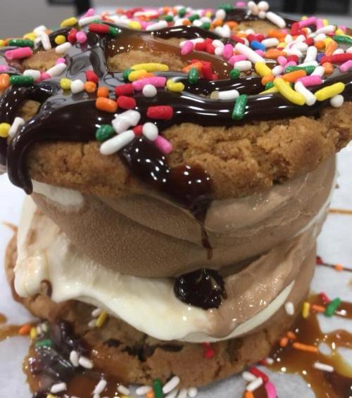 A towering ice cream sandwich made of cookies, chocolate and vanilla ice cream, drizzled with chocolate and caramel, topped with sprinkles.