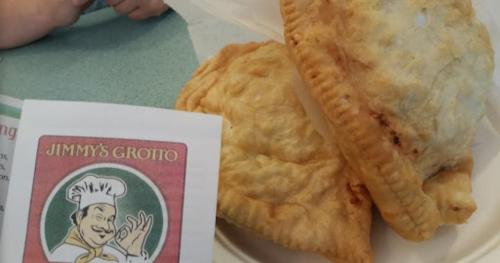 Two golden, flaky pastries on a plate next to a menu featuring a chef logo for Jimmy's Grotto.