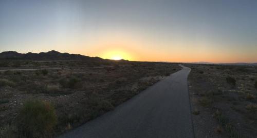 A serene landscape at sunset, featuring a winding road and mountains in the distance under a clear sky.