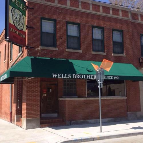 Brick building with green awning reading "Wells Brothers Since 1921" and a street sign in front.