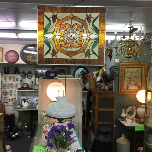 A vintage shop interior featuring a stained glass art piece, antique decor, and various collectibles on display.