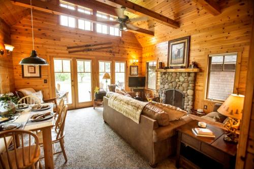 Cozy wooden cabin interior with a stone fireplace, dining table, and large windows letting in natural light.