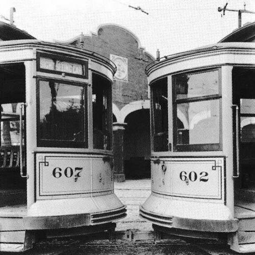 Two vintage trams, numbered 607 and 602, face each other at a station with an archway in the background.