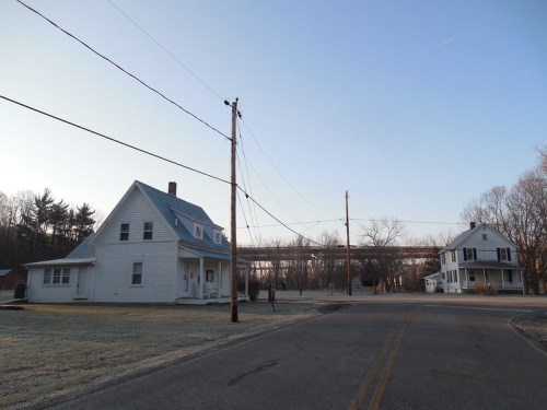 Two white houses at a road intersection, with power lines and a clear sky in the background. Frost covers the ground.