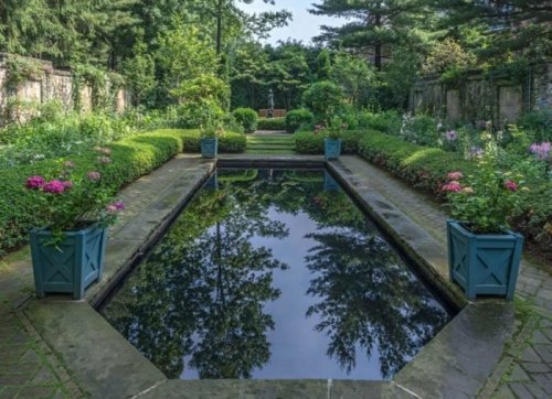 A serene garden with a reflecting pool surrounded by lush greenery and colorful flowers in blue planters.