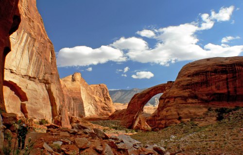 A stunning desert landscape featuring red rock formations and a natural arch under a blue sky with fluffy clouds.