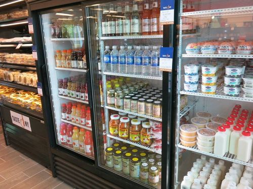 A refrigerated display case filled with various drinks and condiments, including juices, sauces, and yogurt.