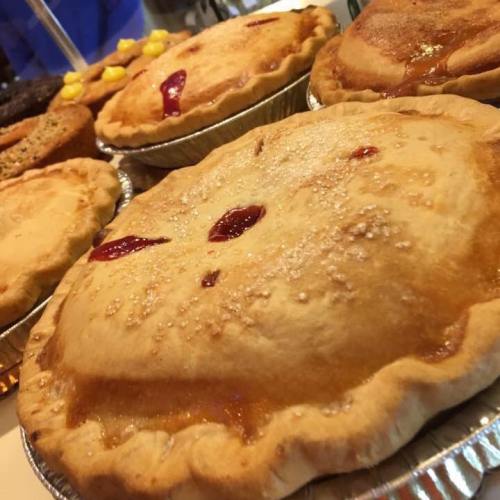 Close-up of golden-brown pies with shiny crusts, some topped with red fruit filling, arranged on a table.