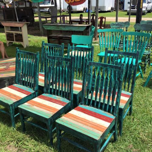 A collection of colorful, rustic wooden chairs with turquoise frames and striped seats, arranged on grass.
